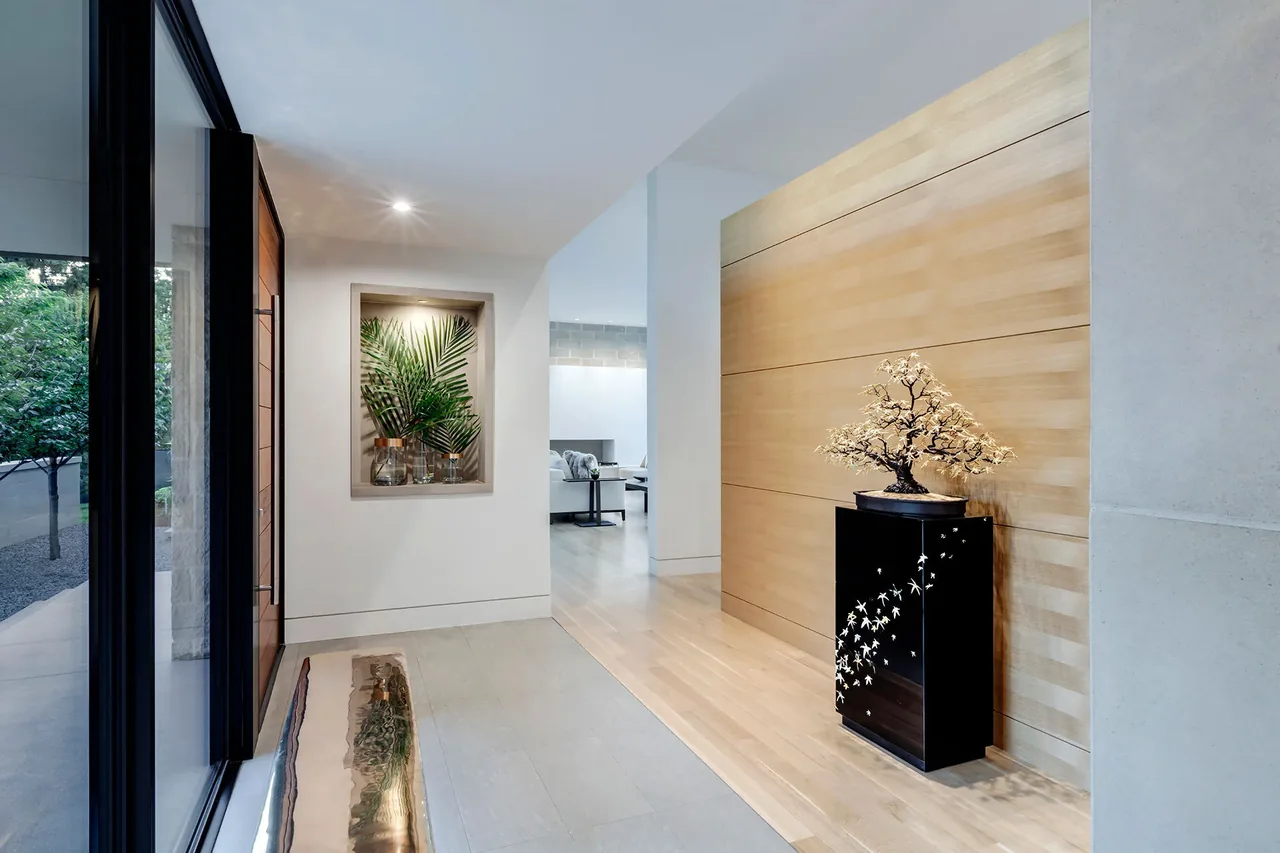 A modern entry hallway featuring a light wood wall panel and a black decorative console topped with a floral sculpture.