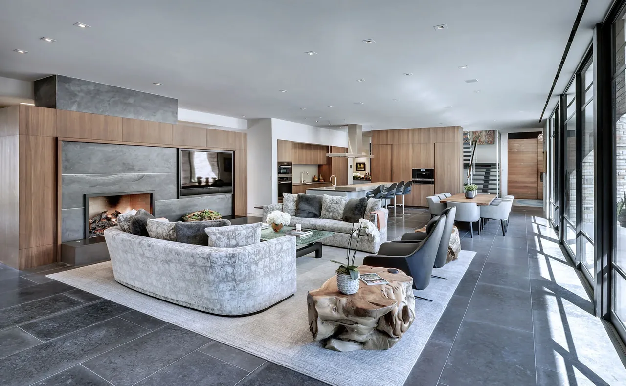 Open concept living, dining, and kitchen space with wood cabinets, stone fireplace surround, and floor-to-ceiling windows.