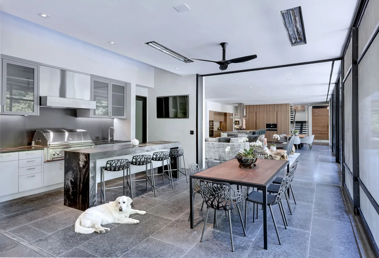 Open kitchen and dining area with a long island, modern chairs, and gray stone tile flooring in the Wildwood I residence.