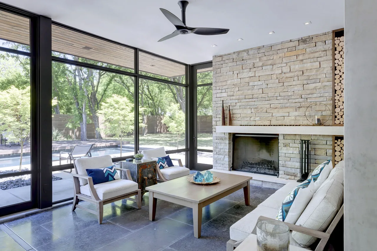 Living room of Wildwood I by BM Architects with stone fireplace, black window frames, and gray stone tile floor
