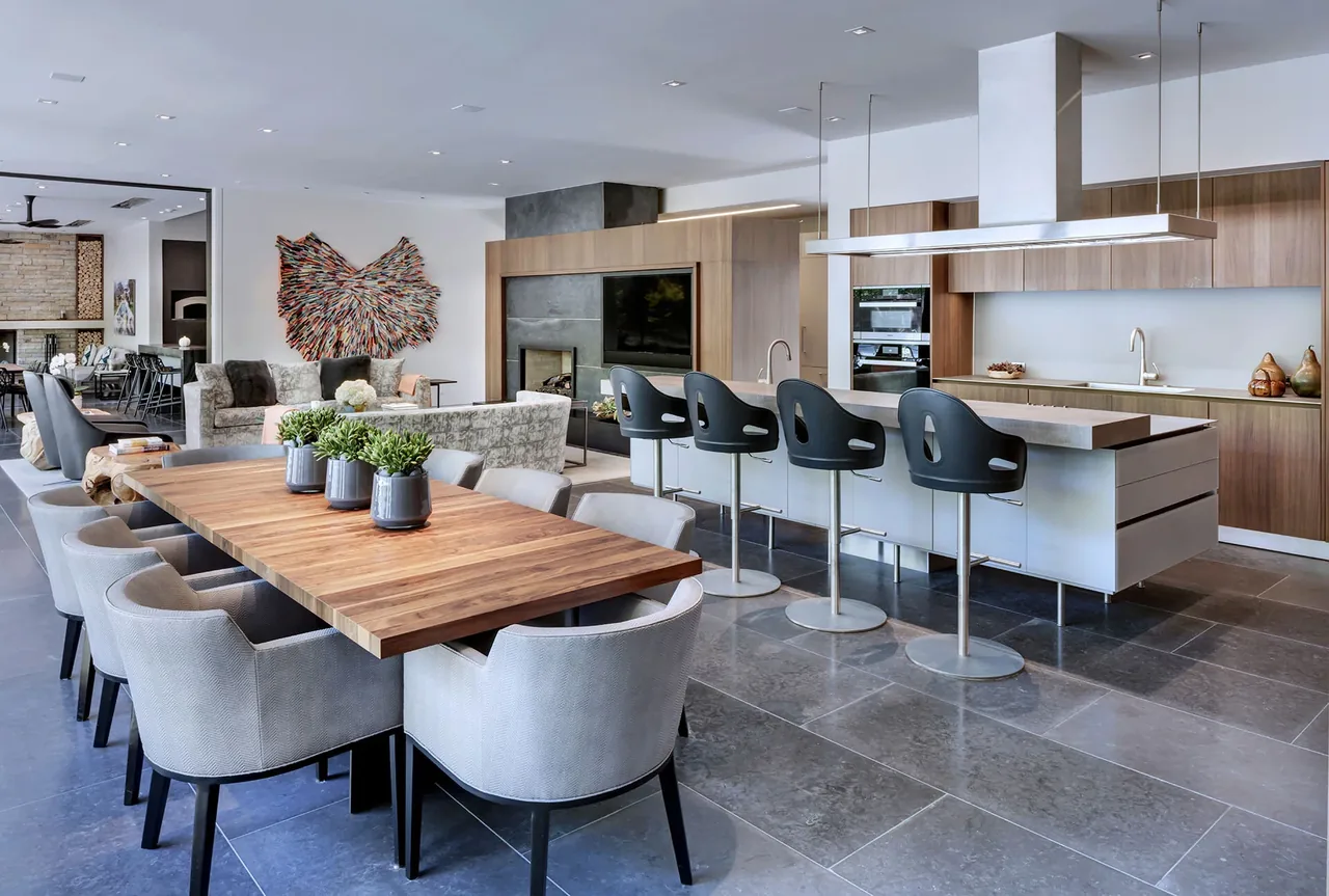 Open kitchen and dining area featuring a wood dining table, modern kitchen island with bar stools, and a living space with a fireplace and wall art.