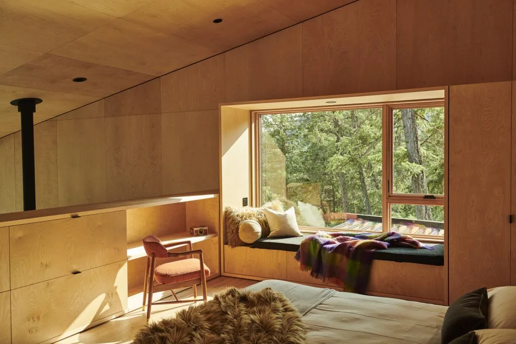 Bedroom featuring a built-in window seat with cushions and a view of the forest through a large corner window.