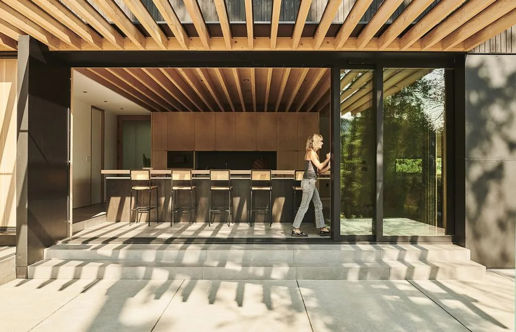 Modern kitchen visible through a large sliding glass door with wood ceiling and cabinetry.