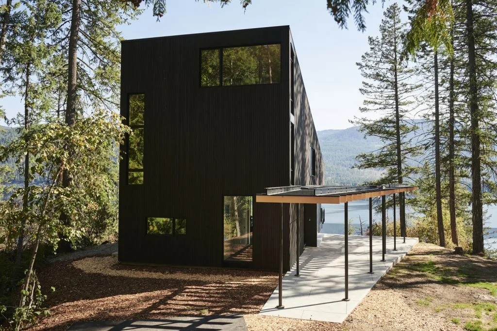Boundary Point Cabin by Bohlin Cywinski Jackson features a vertical wood siding exterior with modern rectangular form in a natural forest setting overlooking water.