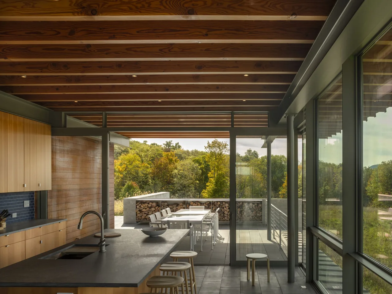 The Gallatin Residence kitchen opens to a covered patio with large glass doors overlooking a green landscape.