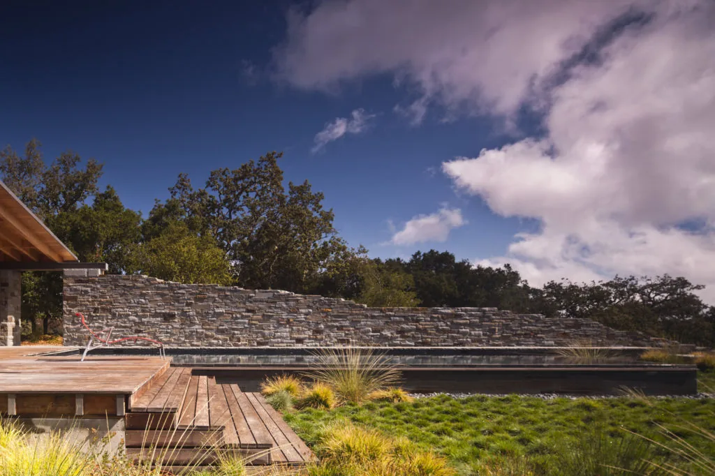 The guesthouse outdoor area includes a wood deck and stone retaining wall with natural landscaping visible beyond.