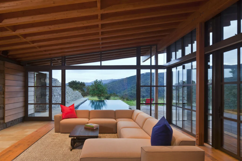 Living room in Halls Ridge Knoll Guesthouse features wood ceiling beams, floor-to-ceiling windows, and views of the pool and landscape.