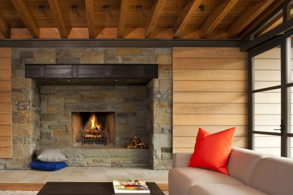 Living room with a stone fireplace, wood ceiling beams, and horizontal wood siding walls at Halls Ridge Knoll Guesthouse.
