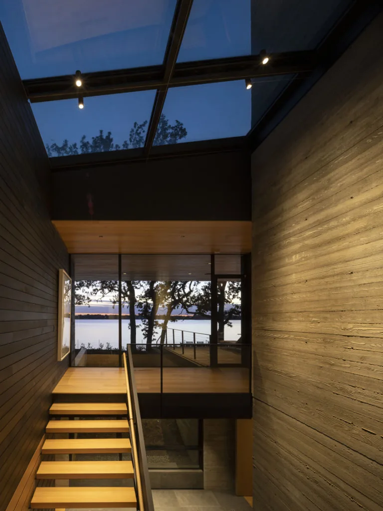 Stairway with wood treads and large glass wall offering water views under a glass skylight.