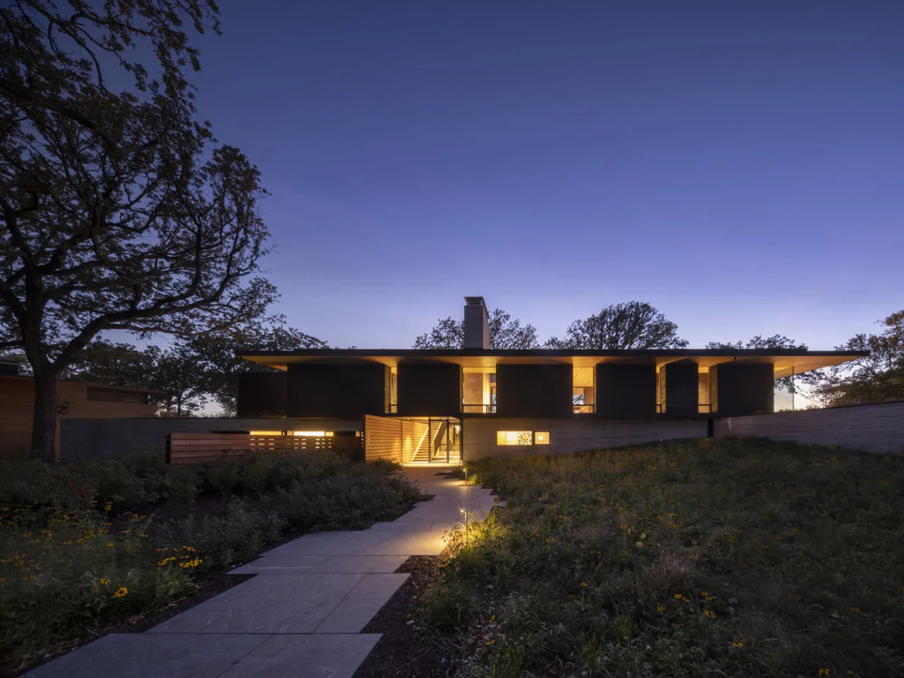 Highbank Residence, a modern home featuring a flat roof and illuminated interior spaces at dusk