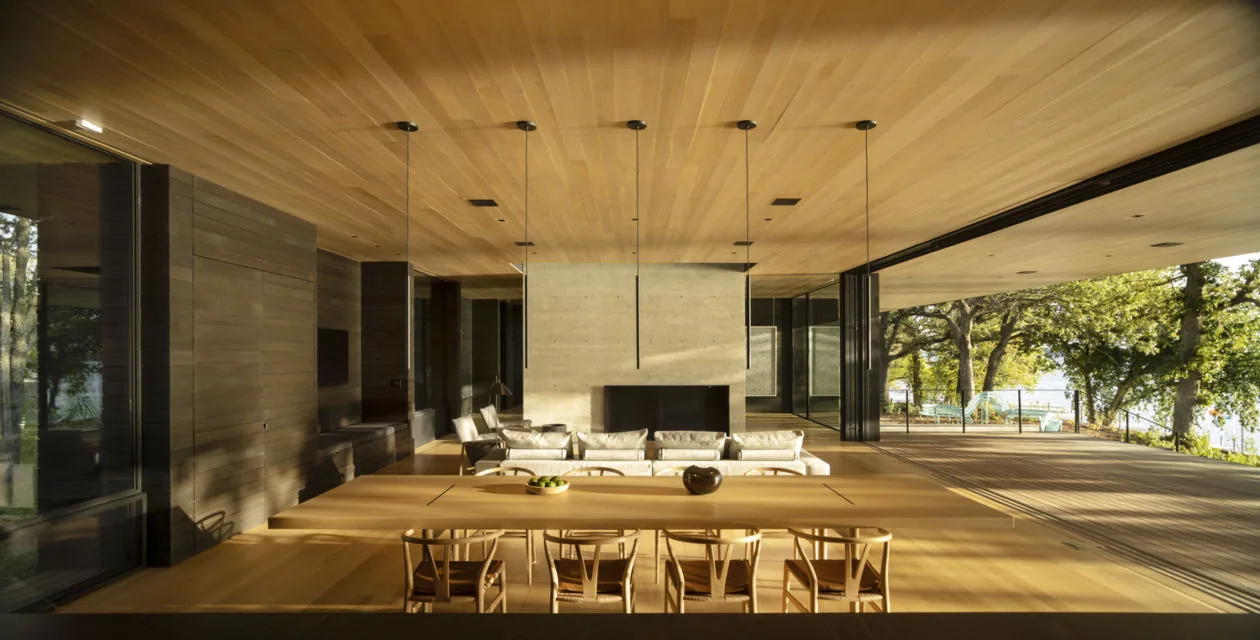 The Highbank Residence features an open interior with wood surfaces, a concrete fireplace, and expansive glass walls connecting to the landscape.