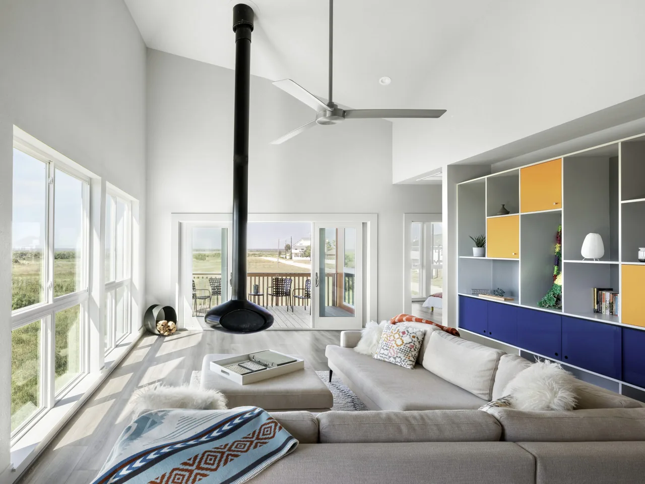 Living room of Arnold Beach House features floor-to-ceiling windows, a suspended fireplace, and bold built-in cabinetry.