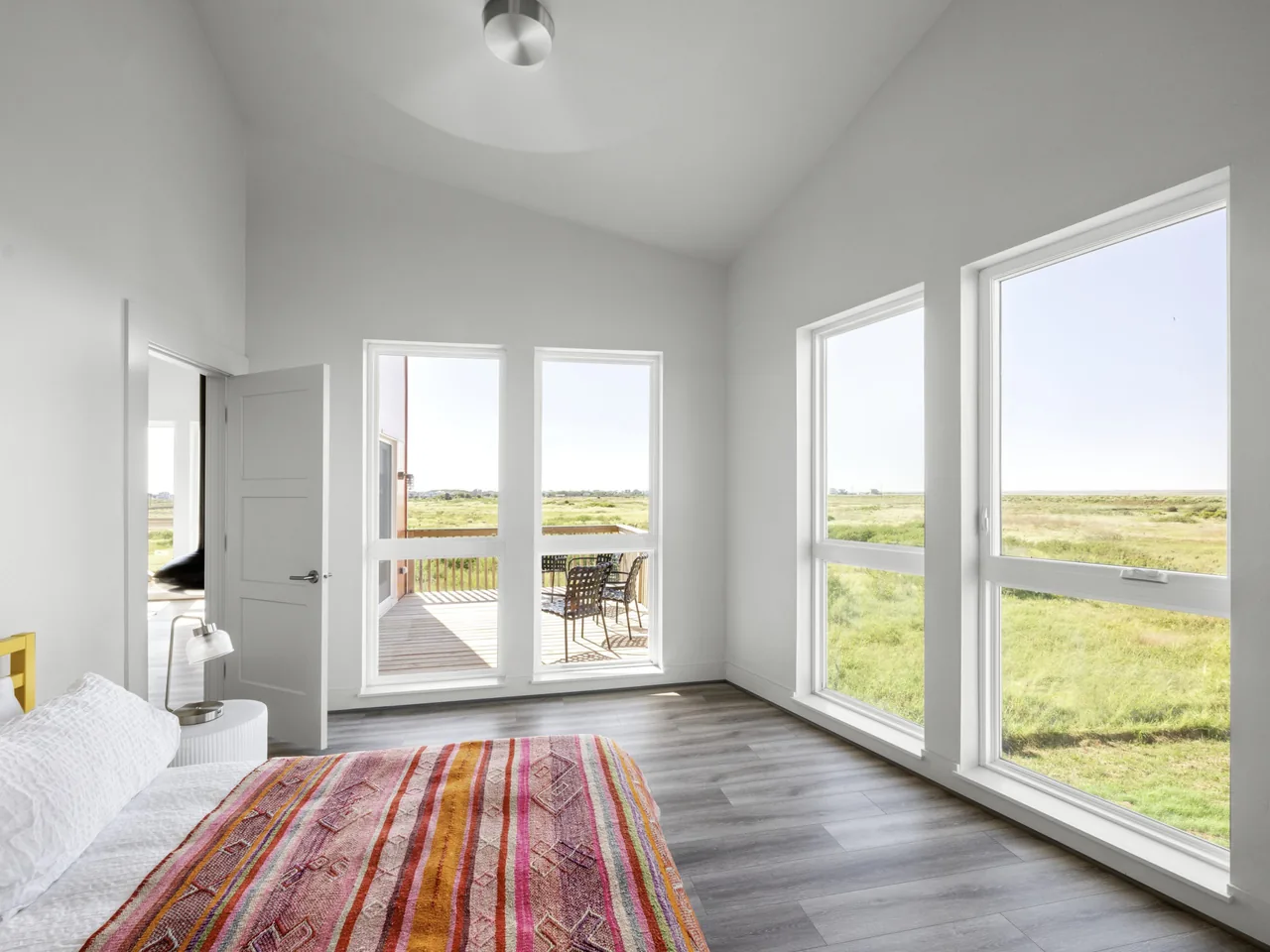 Bedroom features multiple large windows and access to an outdoor deck with seating at the Arnold Beach House.