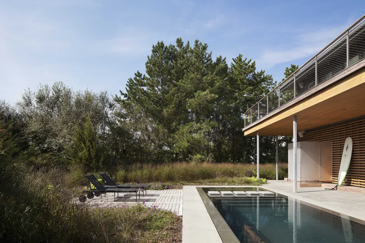 This outdoor living space features a pool and a horizontal wood slat privacy screen under a balcony deck.