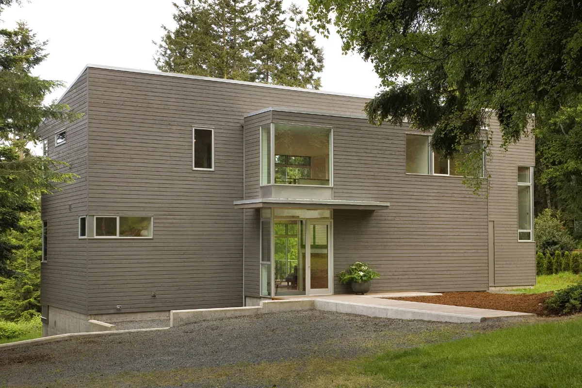 Modern residence featuring horizontal wood siding and various rectangular window sizes in a wooded setting.