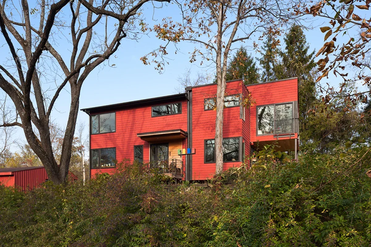 Red two-story modern house with black window frames on a wooded lot.