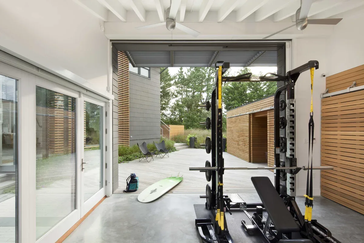 Indoor home gym with weight equipment and open wall leading to an outdoor wood deck with privacy wood slat screens.