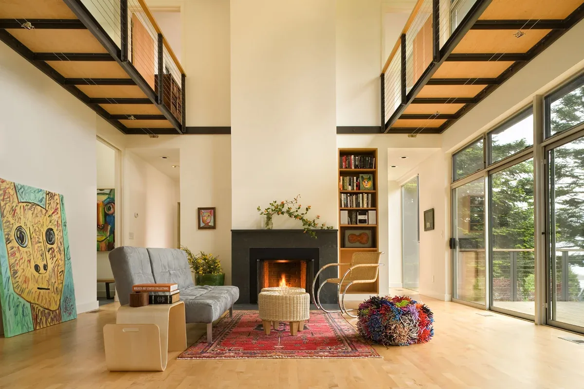Living room in Geist Residence with a fireplace, floor-to-ceiling glazing, and a red area rug under modern seating.