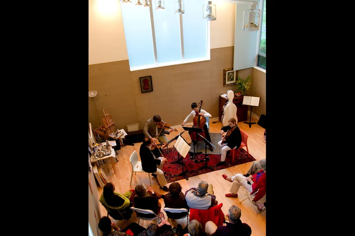 String quartet playing in a residential space with large frosted windows and hardwood flooring at the Geist Residence.