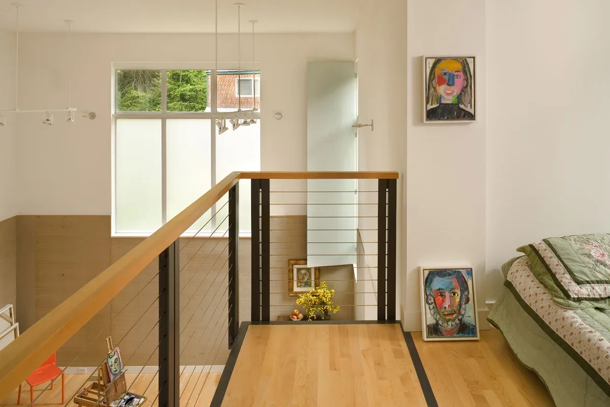 Loft space in the Geist Residence art studio with wood and metal railing and colorful portraits displayed on walls and floors.