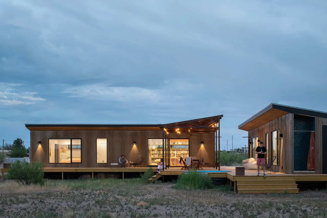 The Marfa zFab house by Brett Zamore Design features wood siding, a covered patio with string lighting, and floor-to-ceiling windows.