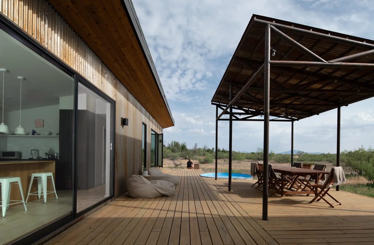 Wooden deck with covered dining area and round pool visible adjacent to a modern rural house.