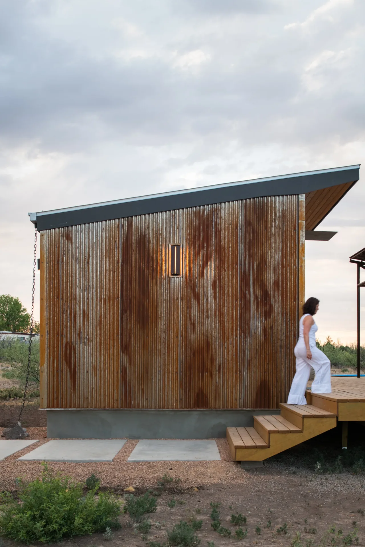 The Marfa zFab project features rusted corrugated metal siding and a shed roof with a raised wooden deck and stairs.