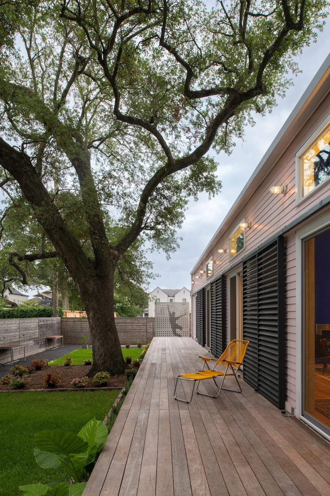 The Pink House features a wooden deck along its side adjacent to a large tree in the garden area.