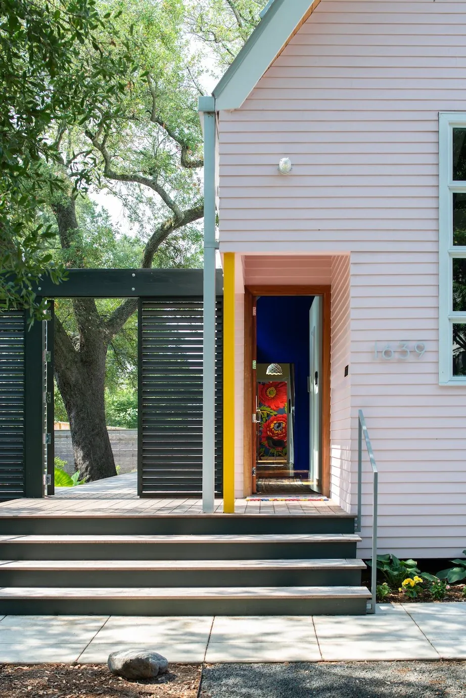 Front entry of The Pink House with black wood gate, steps, and visible colorful interior artwork.