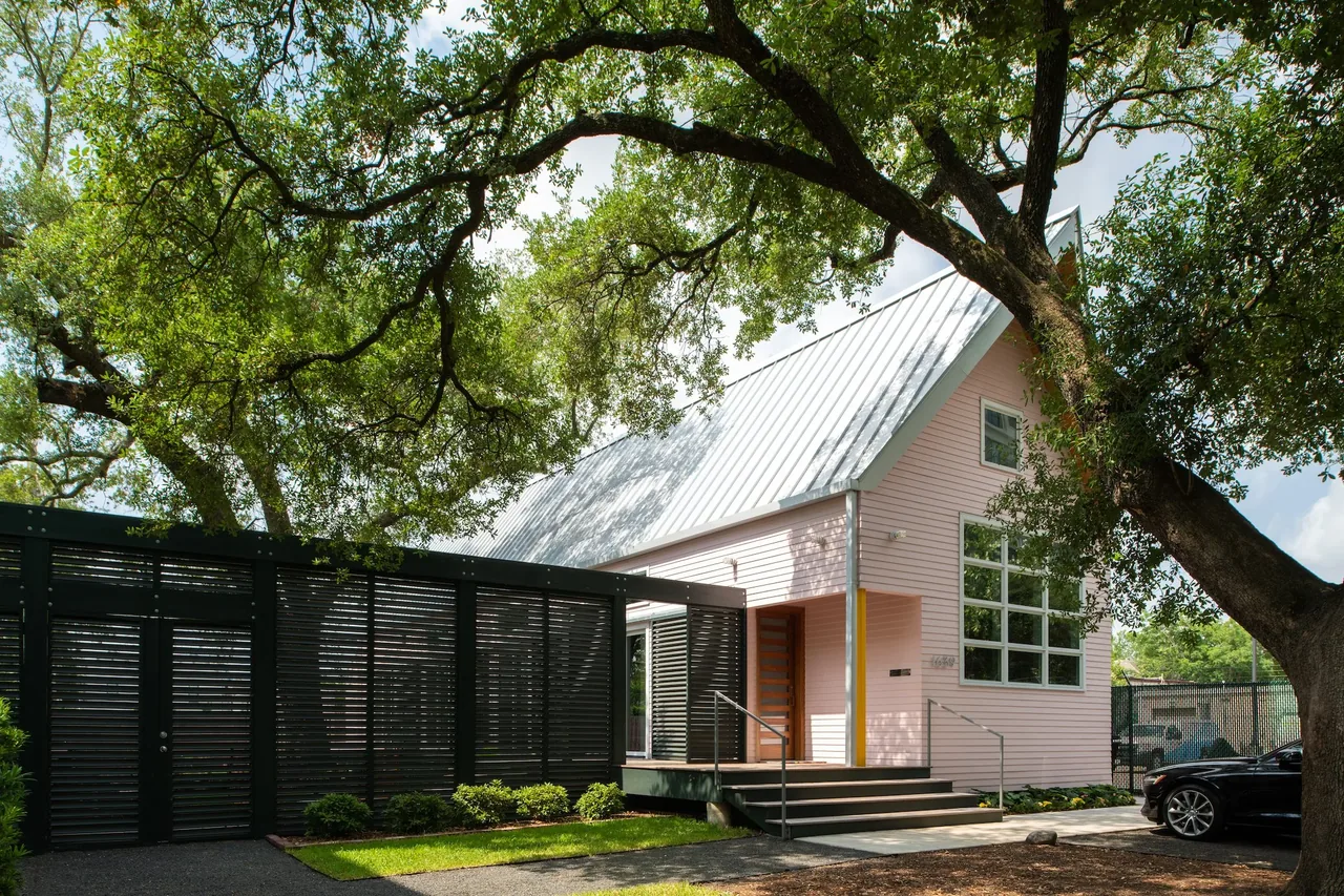 The Pink House features a steep metal roof, large front window, and black front door behind a slatted black fence with front entry steps.