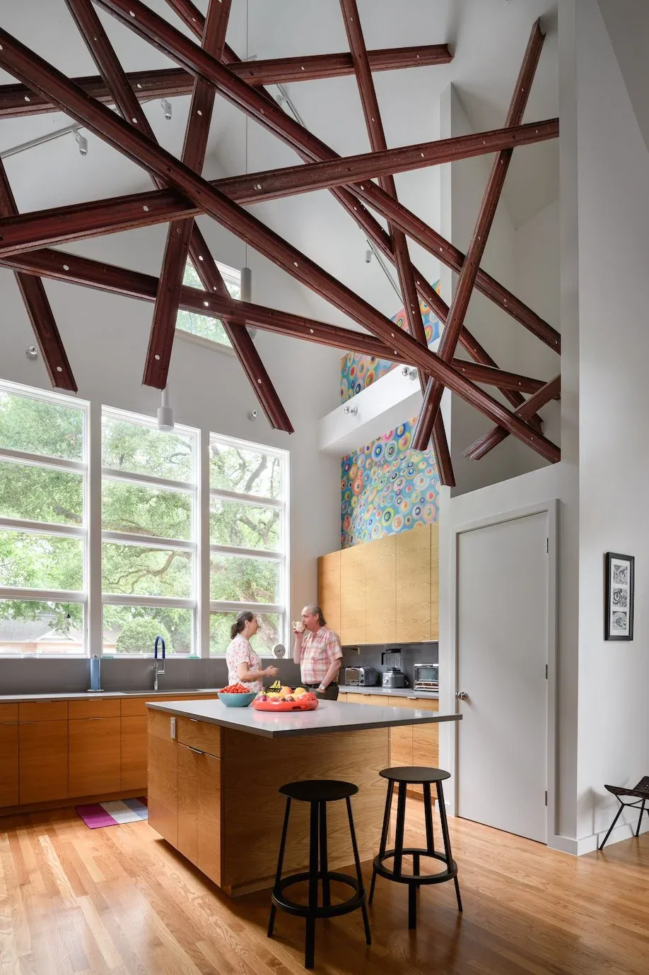 Kitchen interior with exposed wood beams on vaulted ceiling and large grid windows overlooking trees.