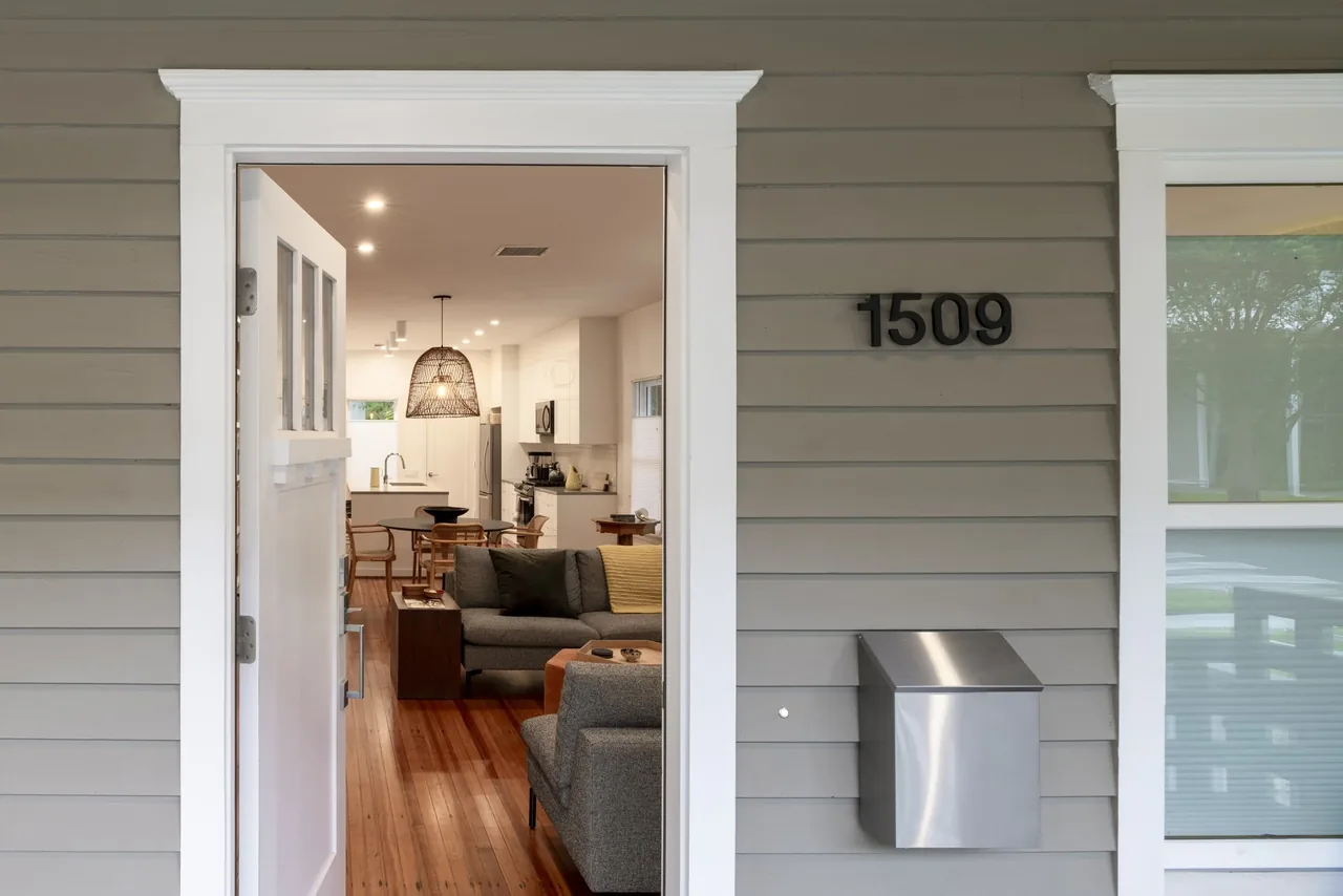 Interior view from the front entry showing a living room with gray furniture and a kitchen with white cabinetry and a woven pendant light.
