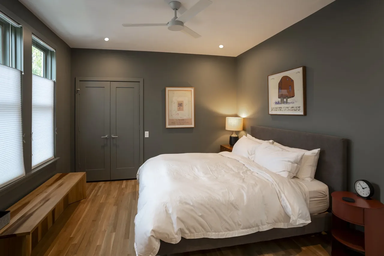 A bedroom features a dark gray color palette with wooden floors, white blinds, and minimalist furniture.