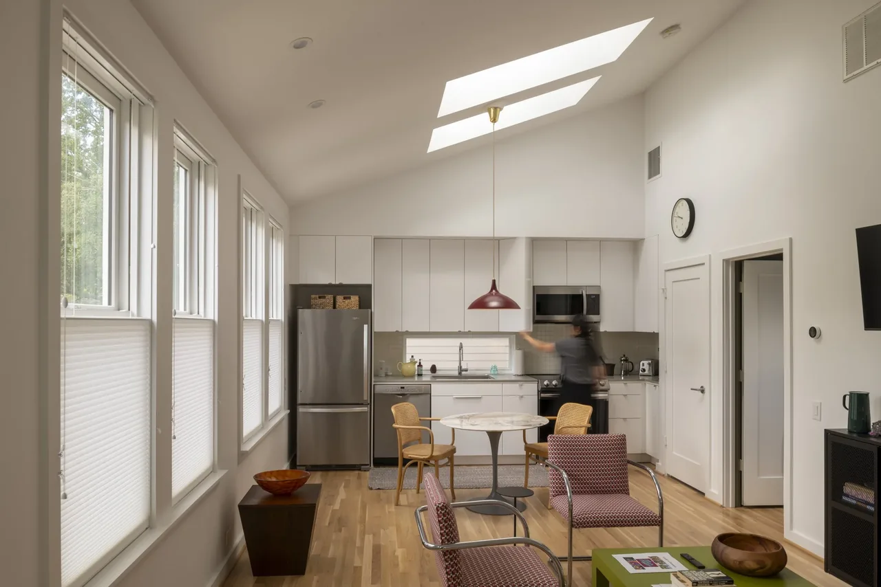 A modern kitchen with white cabinetry, skylights, and a small dining area within an open living space.