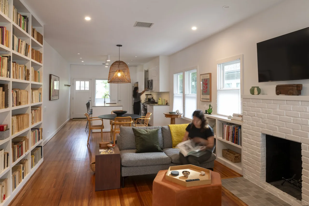 Open living and kitchen area with built-in bookshelves, wood floors, and a woven pendant light over the dining table.