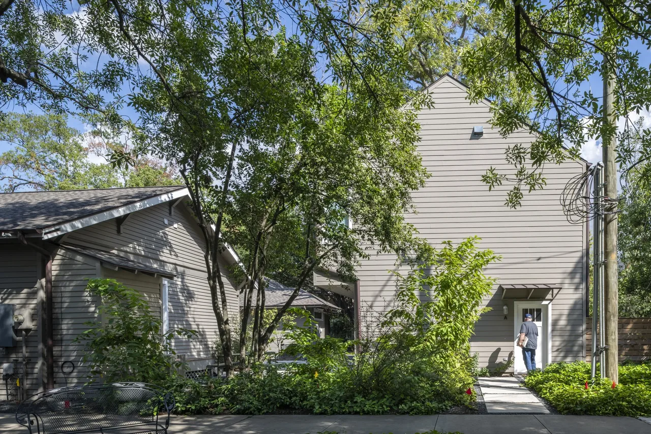 Exterior view of two gray houses with wood siding and gable roofs amidst lush landscaping.