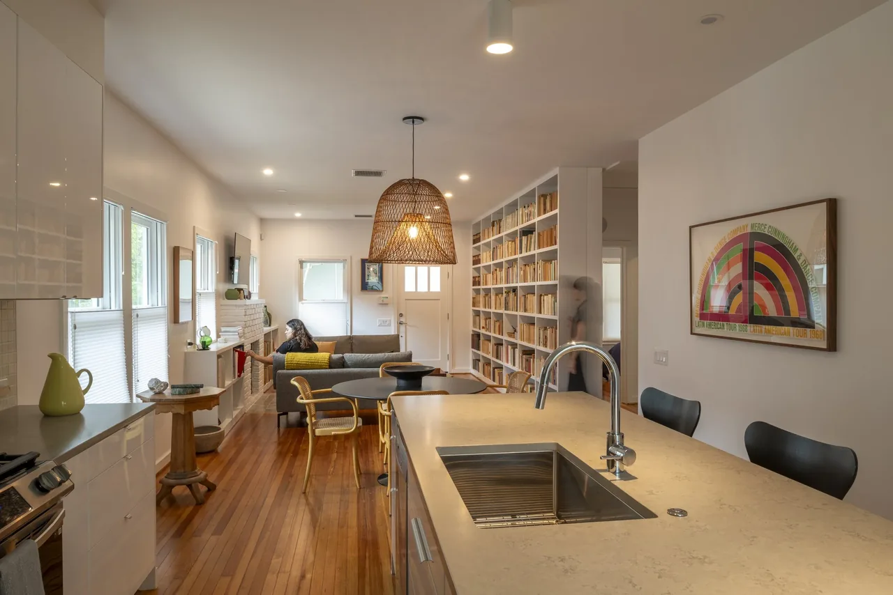 Open-plan kitchen and living room with a large island featuring a sink and woven light fixture overhead.
