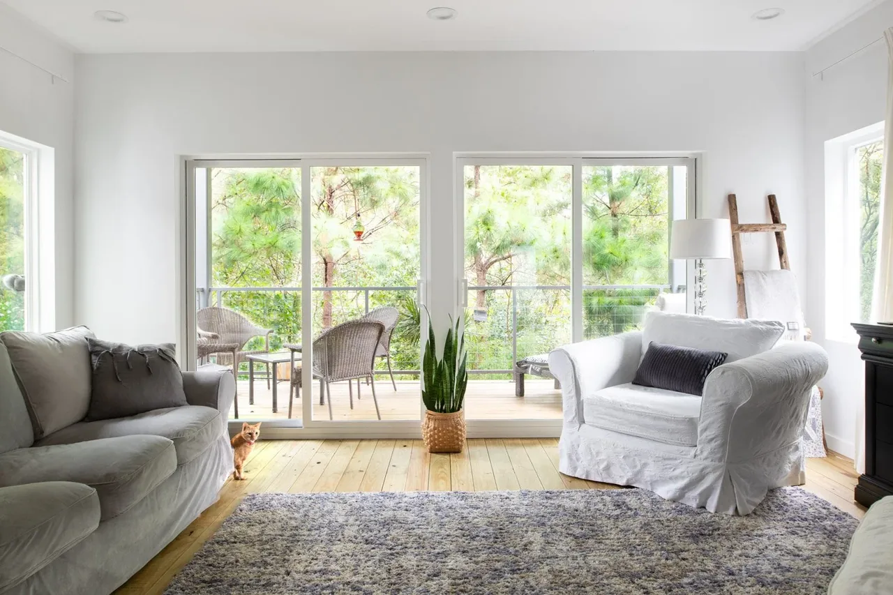 Living room with sliding glass door leading to a balcony with outdoor seating surrounded by greenery.