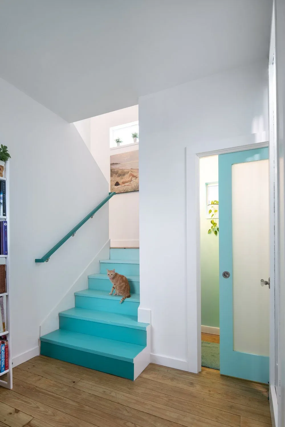 Turquoise-painted stair steps and railing contrast with white walls and wooden flooring inside Saunders House.