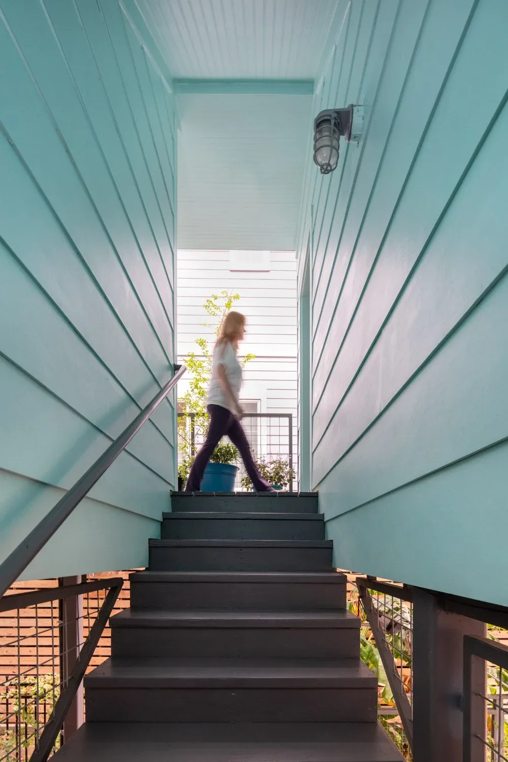 Turquoise exterior stairs with metal railing lead up between two walls clad in horizontal siding at Saunders House.