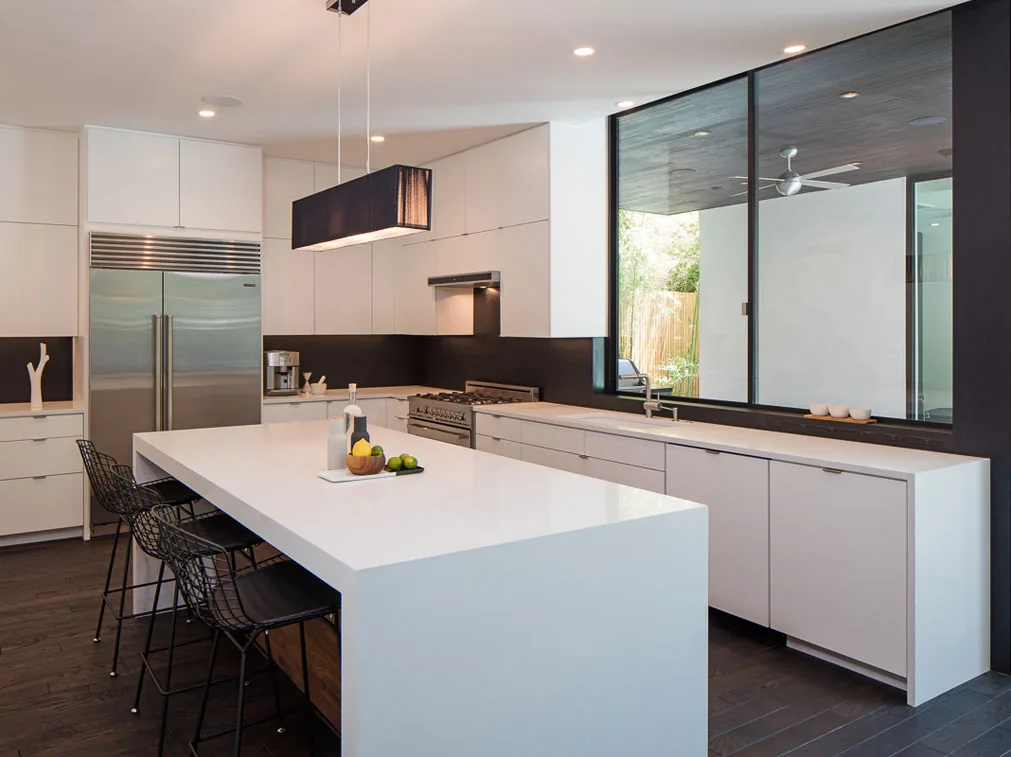 The kitchen features a large white island, black backsplash, and stainless steel appliances with a large window overlooking a covered patio.