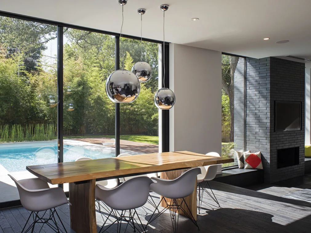 Dining room features a wooden table, modern chairs, and large black-framed glass sliding doors opening to a pool and backyard.