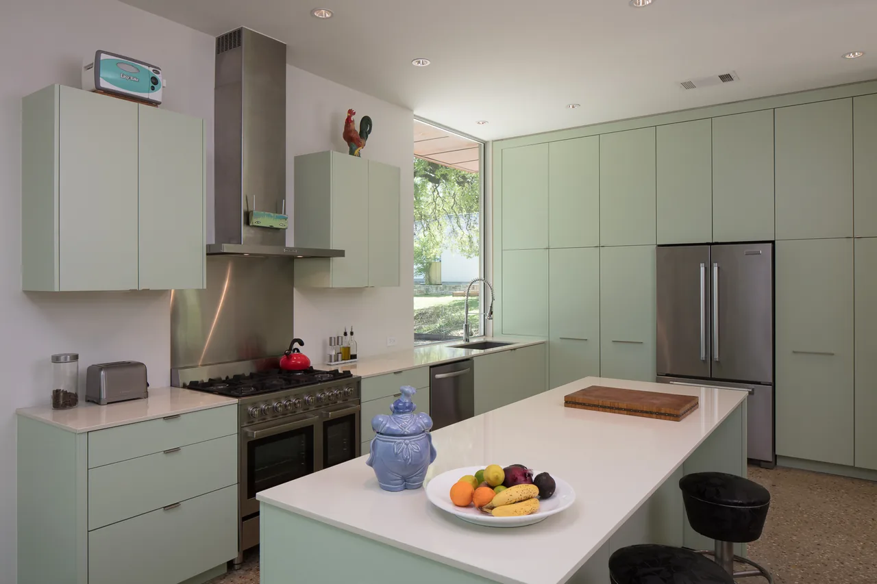 This kitchen features muted green cabinetry, stainless steel appliances, and a large central island under recessed lighting.