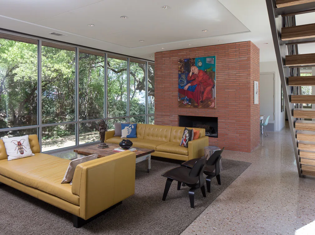 Living room with large glass wall, yellow sofas, and brick fireplace in Bouldin 01 project by Brian Dillard Architecture.