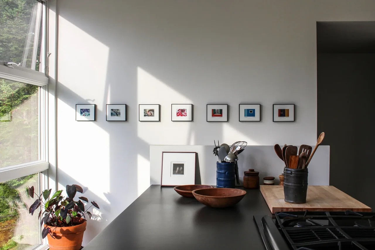 Kitchen counter with utensil holders, wooden bowls, and a row of small framed artworks on the wall above