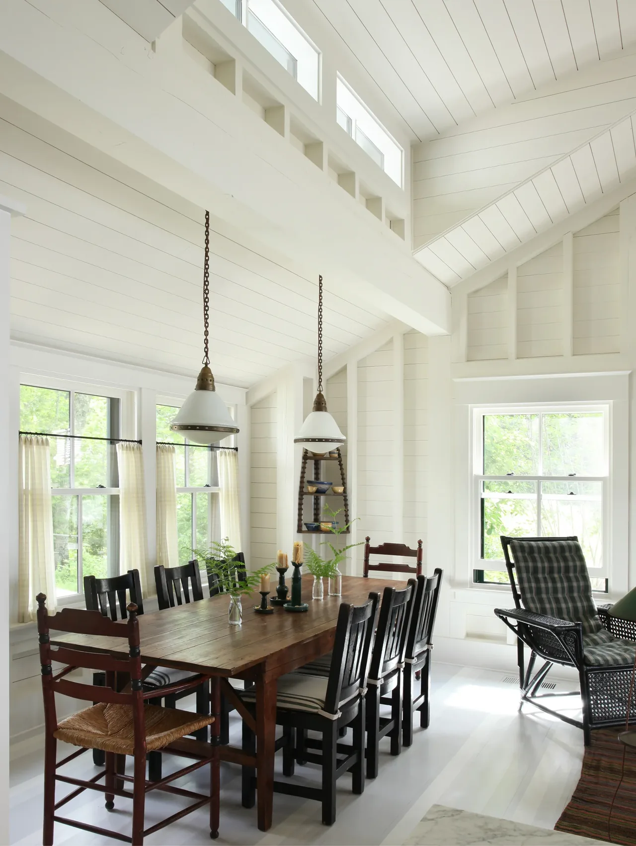 Dining room with a wooden table, mixed chairs, pendant lights, and clerestory windows in a white paneled vaulted ceiling.