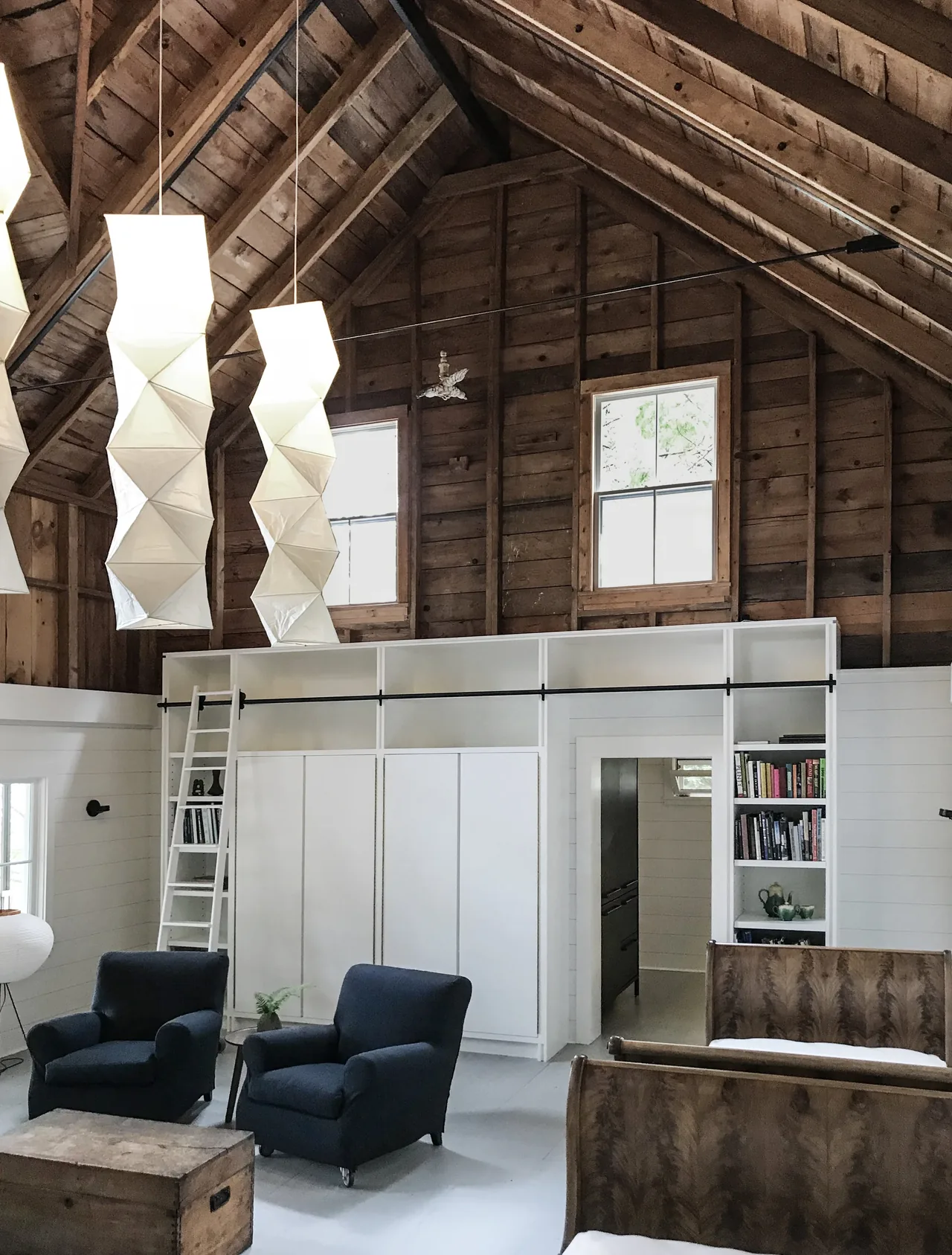 Living area with vaulted exposed wooden ceiling and loft-style shelving accessed by a sliding ladder.