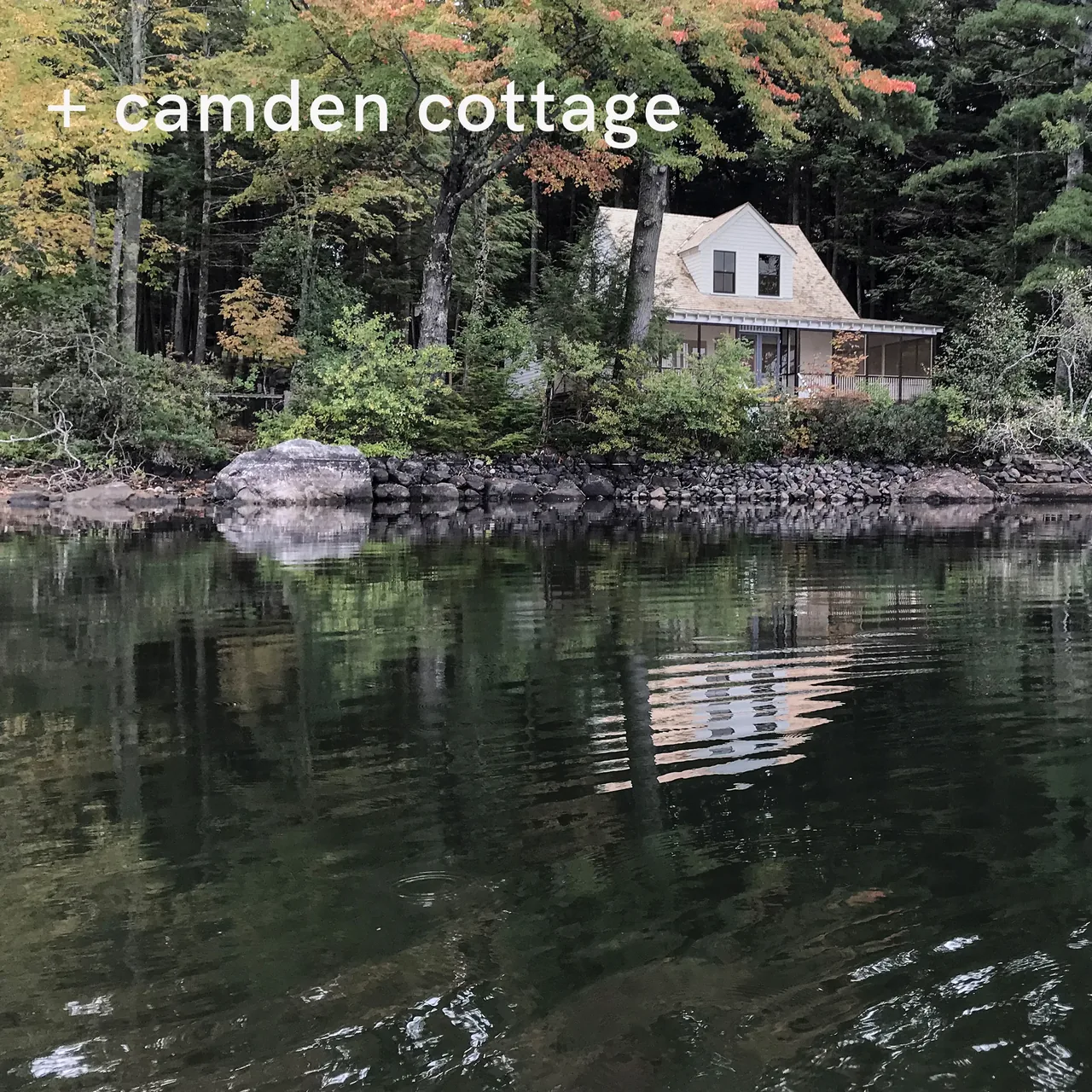 Camden Cottage features a simple gable roof and screened porch, nestled among trees along a lake shore.