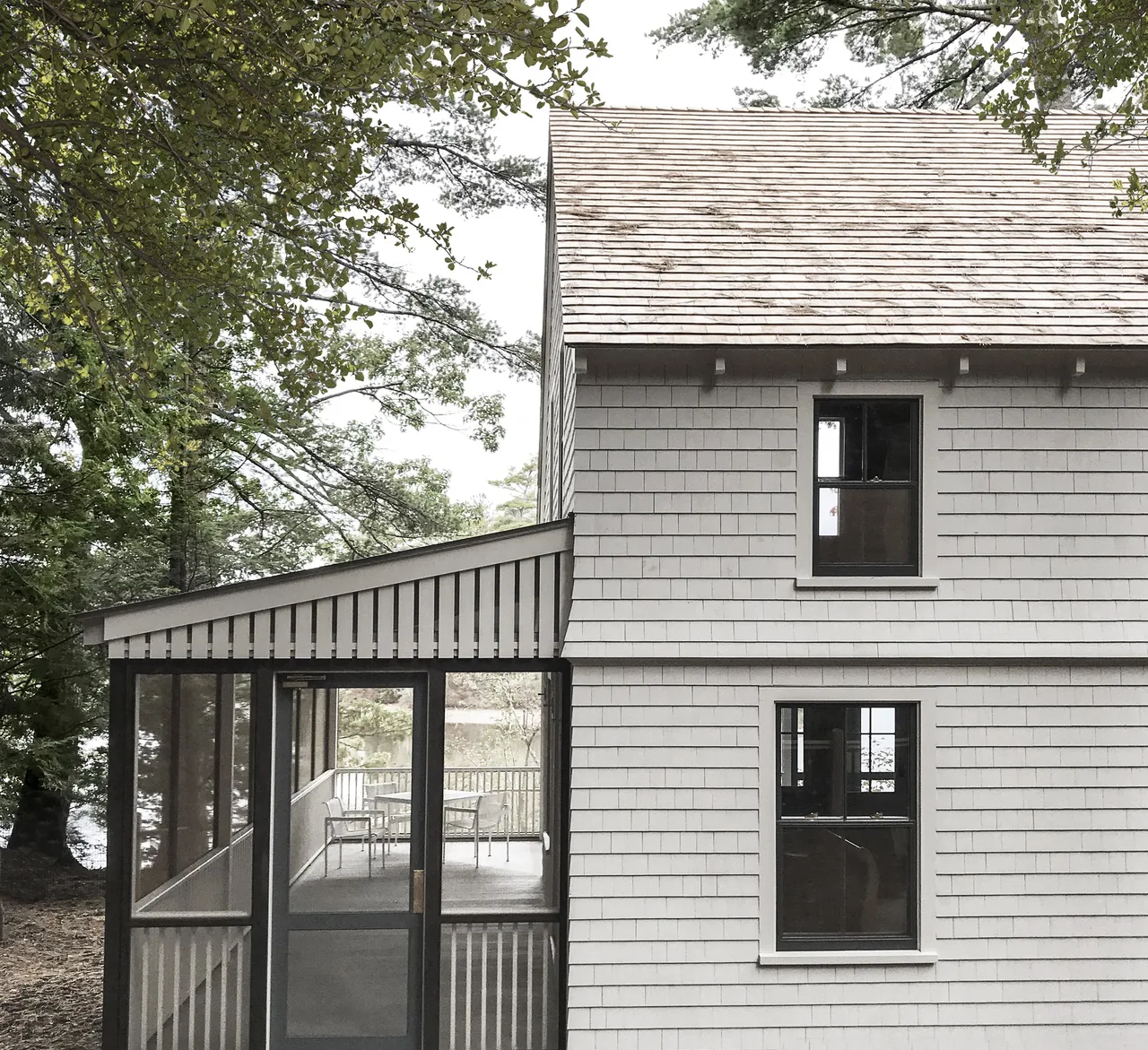 Camden Cottage features shingle siding, black window frames, and a screened porch with a sloped roof.