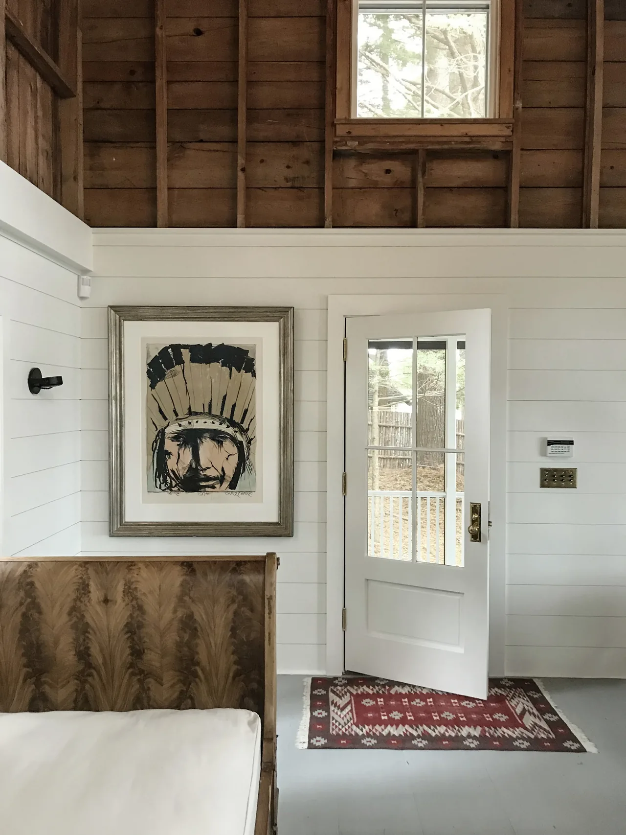 Room interior showing white shiplap, an open glass-paned door, exposed wood ceiling, and framed art above a wooden bench.